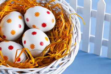 Easter eggs in the basket and white fence on blue background