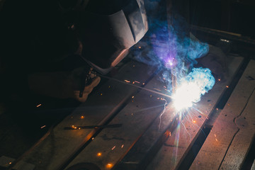 Worker with personal protective equipment and protective mask welding steel pipe in factory.