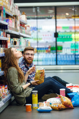 Couple sitting on the supermarket floor and eating snacks