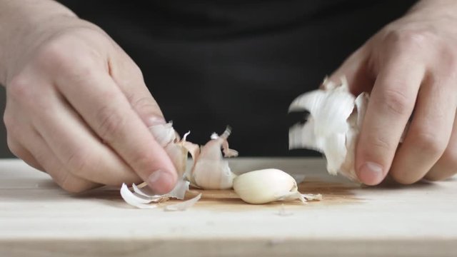 Front view of yong man cook cleans a head of garlic from the husk cutting Board. Closeup shot with natural light