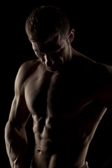 Fototapeta na wymiar silhouette of half-naked handsome and muscular young man posing on a dark background