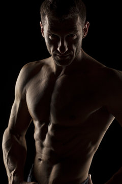 silhouette of half-naked handsome and muscular young man posing on a dark background