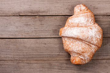 one croissant sprinkled with powdered sugar on old wooden background with copy space for your text. Top view