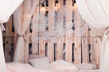 bed with soft cushions and canopies and white dream catcher with the white feathers and pearls hanging on a wooden background.