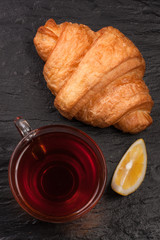 croissant with a cup of tea on a black stone background. Top view