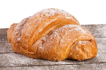 croissant sprinkled with powdered sugar on a wooden table with white background