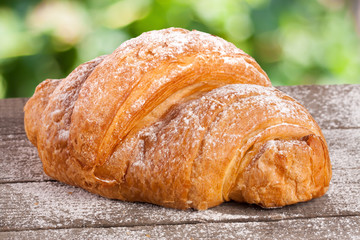 croissant sprinkled with powdered sugar on a wooden board with a blurry garden background