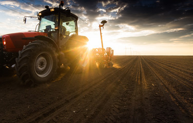 Naklejka premium Farmer with tractor seeding - sowing crops at agricultural field in spring