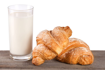 glass of milk with croissant on a wooden table with a white background