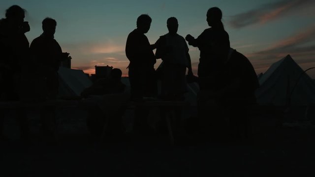 Silhouettes of medieval people who eating at sunset