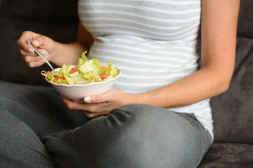 Obraz na płótnie Canvas Close up pregnant woman at home eating a healthy green salad with lettuce, avocado and tomatoes.