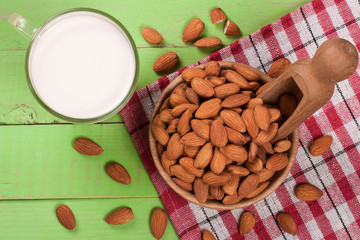 Almond milk in a glass and almonds in a bowl on green wooden background. Top view