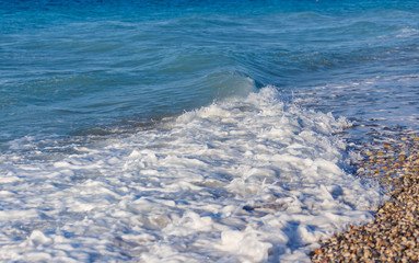 Detailed view of gentle waves lapping against a pebbly beach in Greece Rhodes.