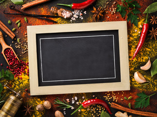 Various spices and herbs surround blank blackboard