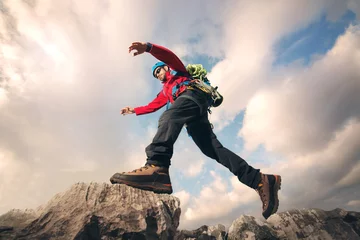 Papier Peint photo Alpinisme Mountaineer jumps over rocks in mountin