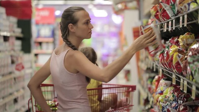 Mother with little daughter choosing snacks in sweets section at the supermarket