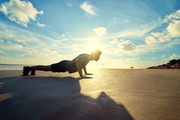 Sports and healthy lifestyle. Young man doing push-ups on the ocean beach.