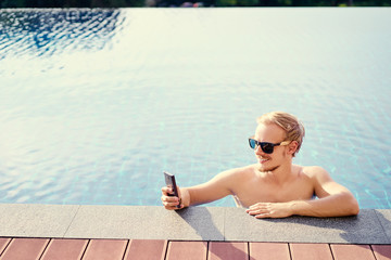 Work and relaxation. Handsome young using smartphone on swimming pool.