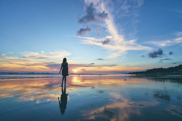 Naklejka premium Niebo i morze. Piękny zachód słońca. Sylwetka młodej kobiety spaceru na plaży oceanu.