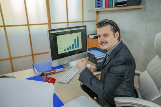 A businessman gives a thumbs up. A chart is seen on the screen. 