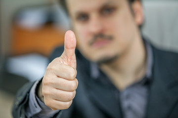 A young man is giving thumbs up and he looks very serious.
