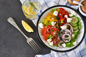 Vegetable mix salad with feta cheese on a black slate background.