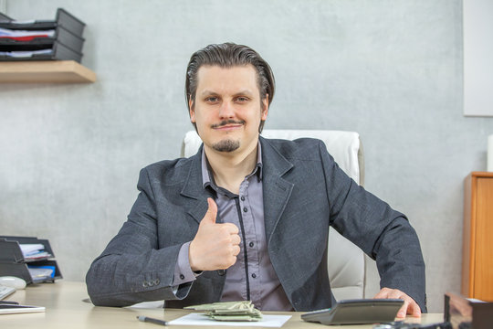 A happy businessman gives a thumbs up and looks happy in his office.