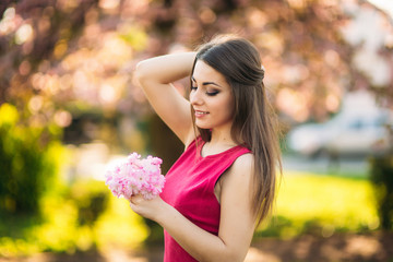 Naklejka premium Beautiful girl posing to the photographer against the background of blooming pink trees. Spring. Sakura.