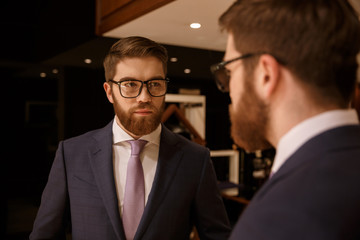 Serious young bearded businessman looking at mirror.