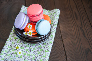 Colorful macarons in a small plate on a wooden background. Close up and copy space.