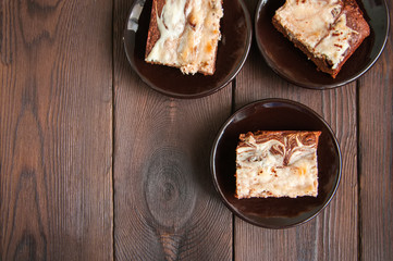 Brownie cheesecake squares in a brown small plates on a wooden background. Close up and top view.
