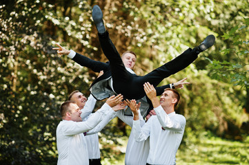 Fashionable groom with four best mans at bow ties outdoor. Friends tossed into the air at theyu...