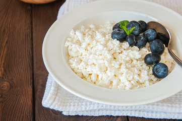 Organic Farming Cottage cheese in a white plate sour cream and blueberries on a wooden background. Copy space.