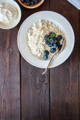 Organic Farming Cottage cheese in a white plate sour cream and blueberries on a wooden background. Copy space.