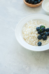 Organic Farming Cottage cheese in a plate sour cream and blueberries on a white stone background. Copy space.