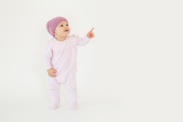 Cute little baby wearing hat standing on floor and pointing.