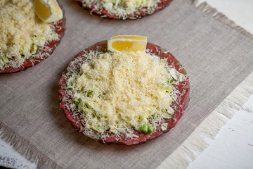 Carpaccio from beef with greens and cheese on a plate on a gray background