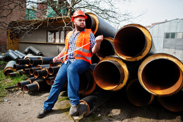 Brutal beard worker man suit construction worker in safety orange helmet near steel pipes with tape...