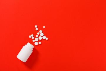 White pills spilling out of a toppled white pill bottle. Isolated on red background. Medicine...