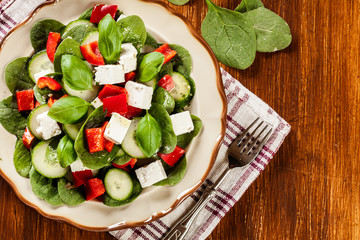 Fresh spinach salad with feta, cucumber and red paprika on a pla