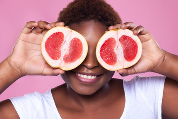 African-American woman with a grapefruit on a pink background,