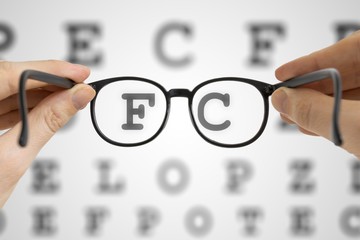 Hands holds black glasses in front of vision testing chart. Eye sight testing concept.
