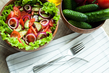 Rustic salad of fresh tomatoes, cucumbers, red onions and lettuce, dressed with olive oil and ground pepper in a wooden bowl. Top view