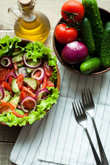 Rustic salad of fresh tomatoes, cucumbers, red onions and lettuce, dressed with olive oil and ground pepper in a wooden bowl. Top view