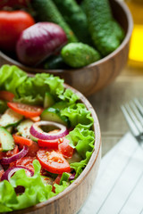 Rustic salad of fresh tomatoes, cucumbers, red onions and lettuce, dressed with olive oil and ground pepper in a wooden bowl. Top view