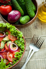 Rustic salad of fresh tomatoes, cucumbers, red onions and lettuce, dressed with olive oil and ground pepper in a wooden bowl. Top view