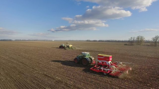 Sowing campaign in early spring. Three tractors pull seeders, aerial 4K video