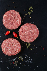 Fresh raw meat burger on the black slate board with herbs and spices for background. Copy space, top view . 