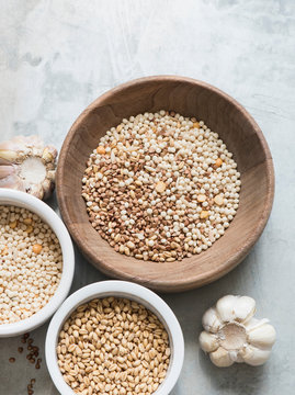 Different types of grains in bowls, garlic bulbs beside bowls, overhead view