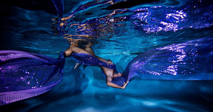 Underwater view of poised woman with wrapped in flowing purple textiles
